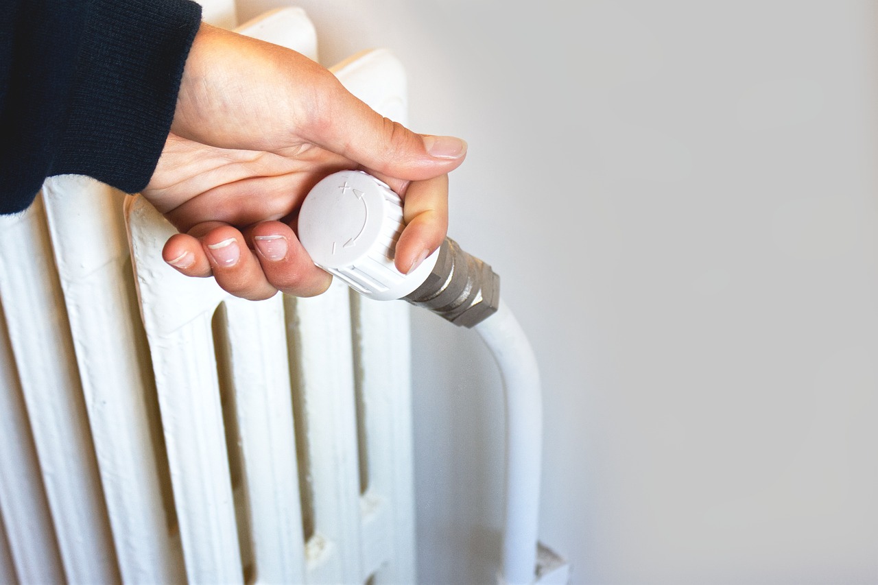 Un homme ajuste la température d'un chauffage afin de réduire la consommation d'énergie.